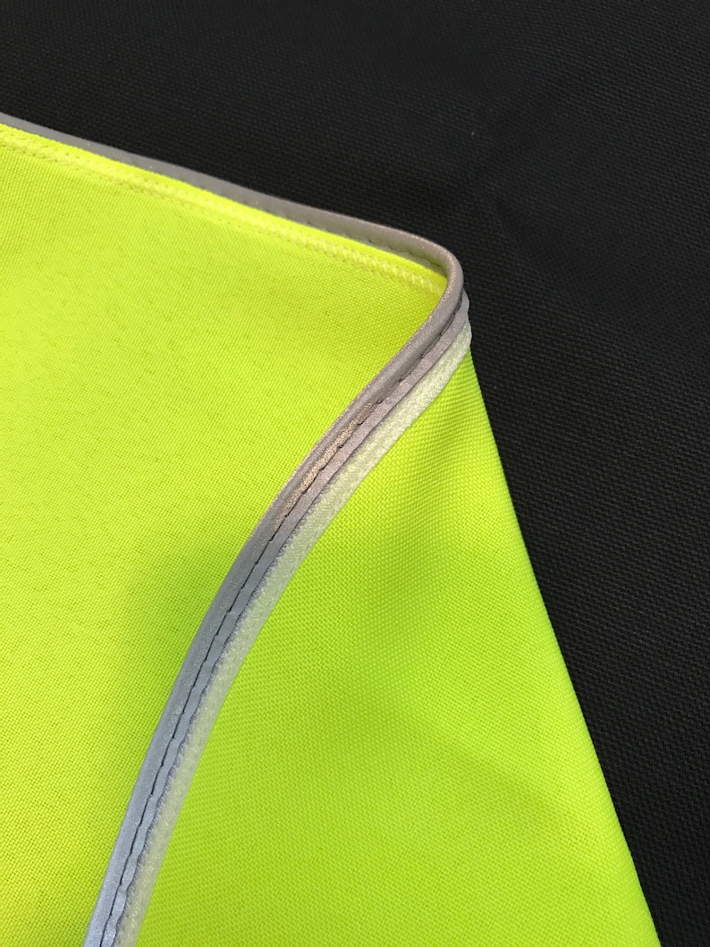 May include: Close-up of a bright yellow fabric with a reflective silver trim. The fabric is folded over and the trim is visible on the edge.