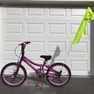 May include: A purple bicycle with pink wheels and a yellow flag with the name "Kierra" on it.
