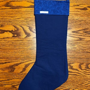 Puede incluir: Una media de Navidad azul oscuro con un pu&ntilde;o estampado en azul y blanco. La media tiene un lazo en la parte superior para colgarla.