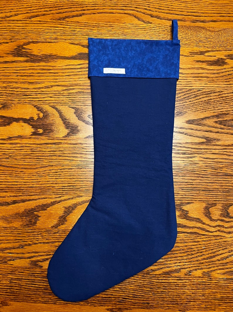 Puede incluir: Una media de Navidad azul oscuro con un pu&ntilde;o estampado en azul y blanco. La media tiene un lazo en la parte superior para colgarla.