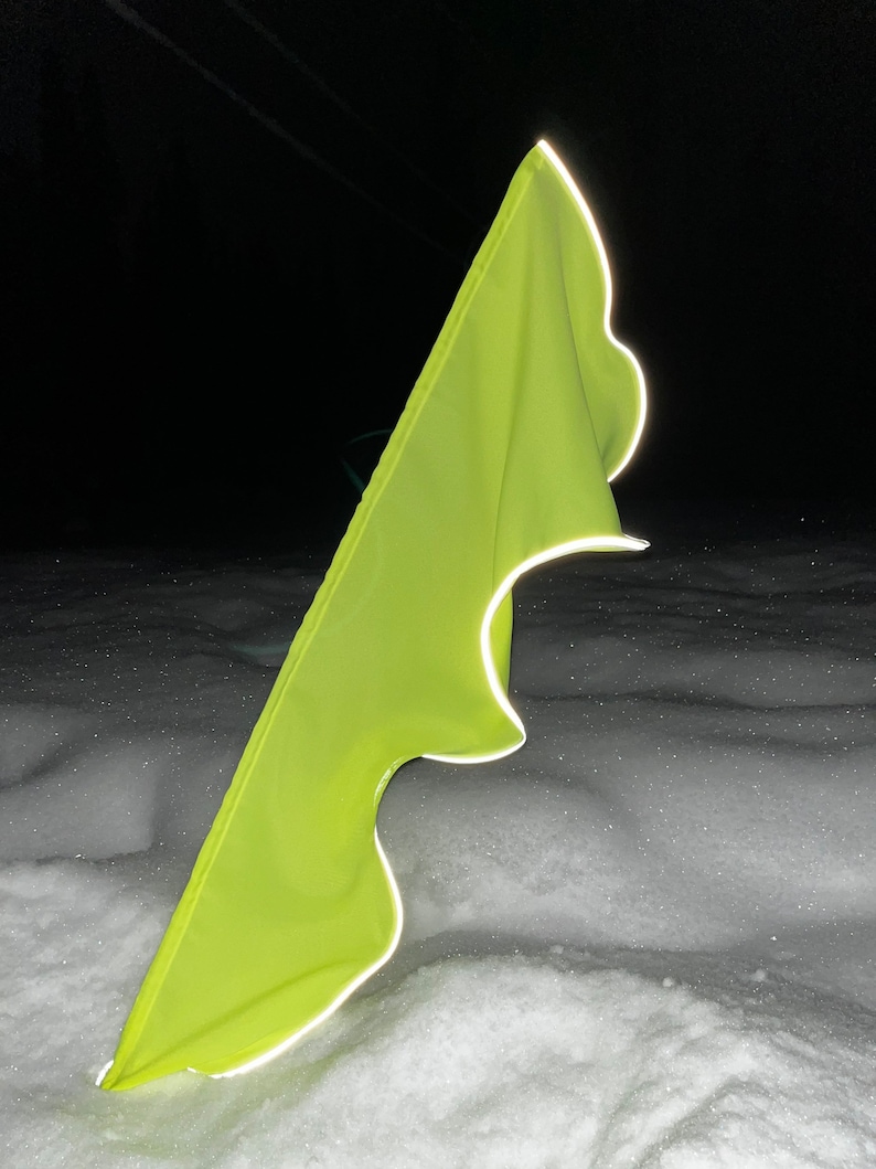 May include: A bright yellow reflective safety flag with a white reflective border, lying in the snow.
