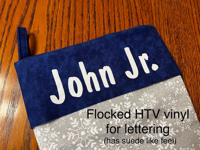 Puede incluir: Una media azul con un patr&oacute;n de copo de nieve blanco y el nombre "John Jr." en letras blancas de vinilo flocado HTV. Las letras tienen una sensaci&oacute;n similar al ante.