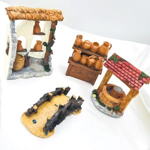 May include: A collection of miniature village figurines, including a well, a shop with pottery, and a bridge. The figurines are made of painted resin and feature a rustic aesthetic with earth-tone colors.