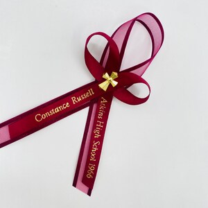 May include: Burgundy ribbon with a gold cross charm and the text "Constance Russell Atkins High School 1966" in gold lettering.