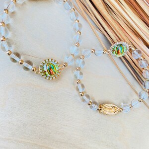 May include: Two clear crystal beaded bracelets with gold accents and a religious charm featuring an image of the Virgin Mary.