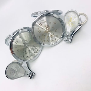 May include: A set of three silver-toned compact mirrors with a princess design and a silver-toned nail clipper with a princess design. Each mirror has a silver background with a gold princess design and gold stars.