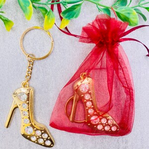 May include: A gold high heel shoe keychain with rhinestones, packaged in a red organza bag.