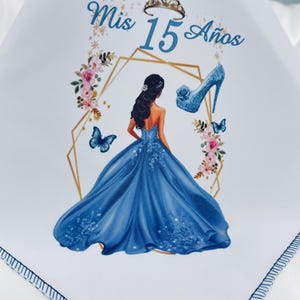 May include: White handkerchief with a blue and gold design. Features a blue gown, high heel, butterflies, and the text "Mis 15 Años". Includes a gold tiara and floral accents. The handkerchief has a stitched border.
