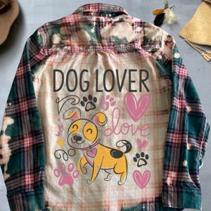 May include: A green and pink plaid flannel shirt with a bleached effect. The back of the shirt features a cartoon dog with the text "DOG LOVER" and hearts.