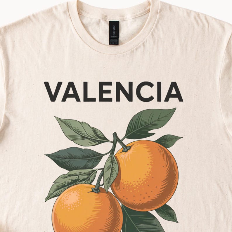 May include: A white t-shirt with the word "VALENCIA" printed in black letters. The shirt features a graphic of two orange oranges on a branch with green leaves.