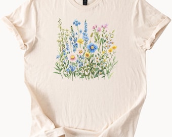 Op de afbeelding: Crèmekleurig T-shirt met een aquarel bloemenontwerp. Het ontwerp toont een verscheidenheid aan wilde bloemen in tinten blauw, geel, roze en wit, met groene bladeren. Het shirt heeft een klassieke ronde hals en korte mouwen.