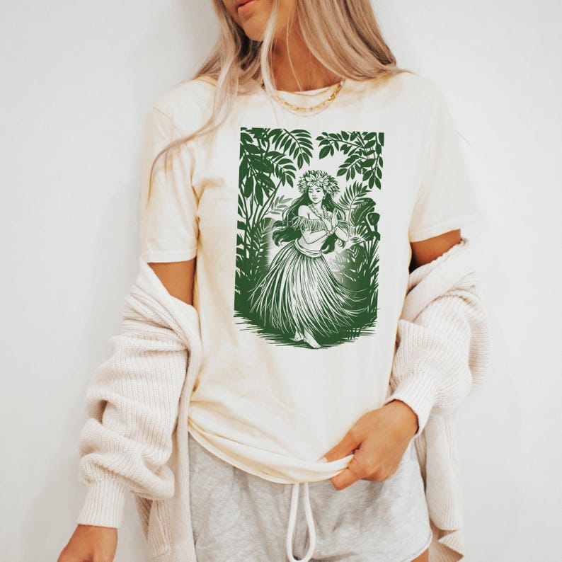 May include: A white t-shirt with a green print of a hula dancer in a tropical setting. The dancer is wearing a flower crown and a grass skirt.