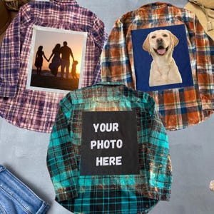 May include: Three flannel shirts with different designs. The first shirt is purple and white plaid with a photo of a family on the back. The second shirt is orange and black plaid with a photo of a dog on the back. The third shirt is blue and black plaid with the text "YOUR PHOTO HERE" on the back.