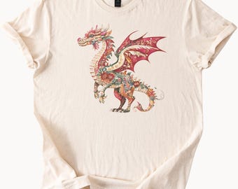 May include: Cream-colored t-shirt featuring a detailed illustration of a dragon. The dragon is adorned with floral patterns in shades of red, pink, yellow, and green. The dragon's wings are a deep red, and the overall design is intricate and eye-catching.