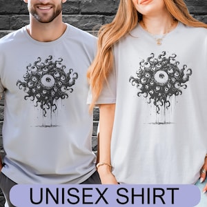 Puede incluir: Dos camisetas unisex de color gris claro con un gráfico negro de un grupo de ojos. Las camisetas tienen cuello redondo y mangas cortas. El texto "UNISEX SHIRT" se muestra en la parte inferior de la imagen.