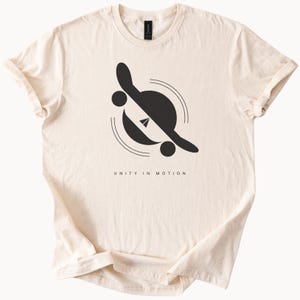 May include: A cream-coloured t-shirt with a black graphic of a skateboard in a circle with the text "UNITY IN MOTION".