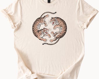 May include: A cream-colored t-shirt with a graphic print of two tigers facing each other in a circle.