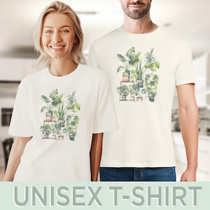 Puede incluir: Camisetas unisex color crema con una ilustraci&oacute;n de acuarela de plantas en macetas. El dise&ntilde;o incluye helechos, palmeras y otras plantas verdes sobre estanter&iacute;as de madera. El texto "UNISEX T-SHIRT" se muestra en la parte inferior de la imagen.