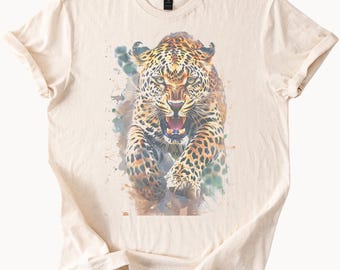 May include: Cream-colored t-shirt featuring a watercolor illustration of a snarling leopard. The leopard is depicted with orange, brown, and black spots, with its mouth open, revealing its teeth. The design includes blue and green watercolor splashes.