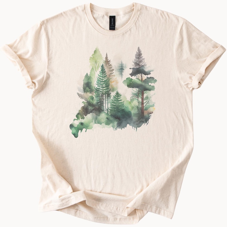 May include: A cream-colored t-shirt with a watercolor design of a forest scene. The design features green and blue trees with a white background.