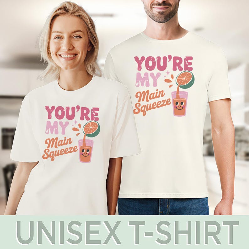 K&ouml;nnte beinhalten: Zwei Personen tragen passende cremefarbene Unisex-T-Shirts. Die Shirts zeigen den Text "YOU'RE MY Main Squeeze" in Pink und Orange sowie eine Grafik eines Saftglases und einer Zitrusfrucht. Der untere Teil des Bildes lautet "UNISEX T-SHIRT".