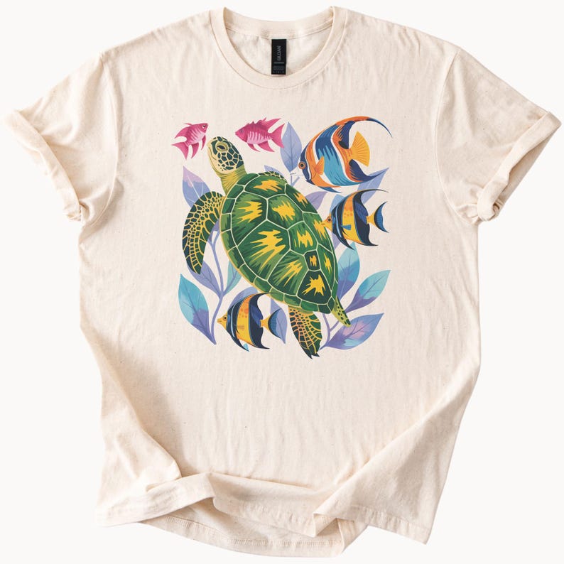 May include: Cream-coloured t-shirt with a colourful illustration of a green sea turtle with yellow details, surrounded by fish and blue and purple leaves. The design is centred on the front of the shirt.