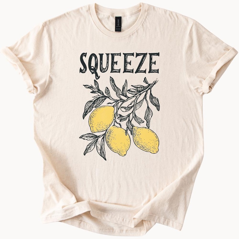 May include: A beige t-shirt with the text "Squeeze" printed in black. A black and white illustration of lemons on a branch is below the text.