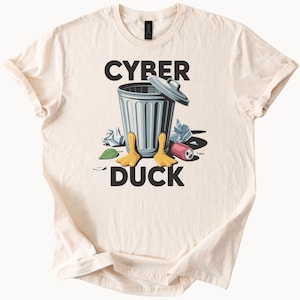面白いサイバーダックゴミ箱グラフィックTシャツ。漫画のアヒルの脚とテクノロジーの残骸が描かれており、オタクやナードスタイルの服装にぴったりのユーモアシャツです。