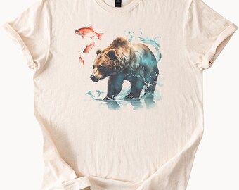 May include: A beige t-shirt with a watercolor illustration of a brown bear standing in water with orange fish swimming around it.