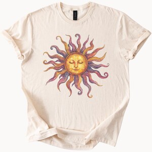 May include: A cream colored t-shirt with a colorful sun graphic. The sun has a face with closed eyes and a yellow, orange, and red color scheme.