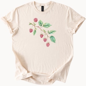 May include: A cream colored t-shirt with a watercolor illustration of a raspberry branch with green leaves and pink raspberries.