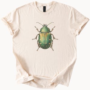 May include: A beige t-shirt with a green and white beetle illustration printed on the front.