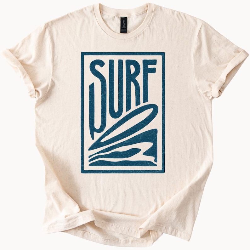 May include: A cream colored t-shirt with a blue graphic of the word "SURF" with a stylized wave design.
