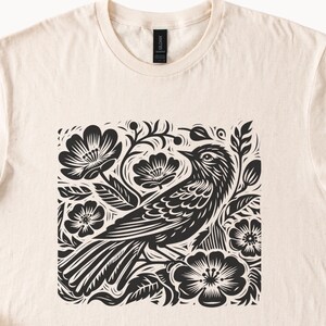 May include: A black and white illustration of a bird perched on a branch with flowers. The design is in a square shape and has a folk art style.