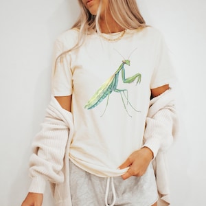 May include: A white t-shirt with a green praying mantis illustration printed on the front.