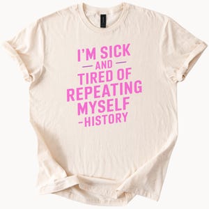 May include: A beige t-shirt with pink text that reads "I'm sick and tired of repeating myself - history".