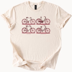 May include: A beige t-shirt with a vintage illustration of four bicycles in shades of red. The bicycles are labeled with their names and types.