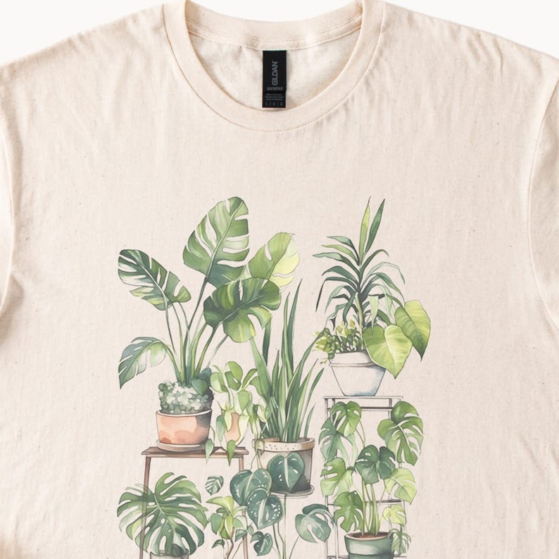 Puede incluir: Camiseta de color crema con una ilustraci&oacute;n de acuarela de varias plantas en macetas. El dise&ntilde;o incluye varios tipos de plantas verdes de hojas en macetas de terracota y blancas, dispuestas en estantes de madera. La camiseta tiene cuello redondo.