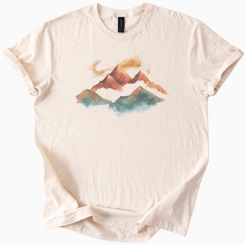 Op de afbeelding: Een cr&egrave;mekleurig T-shirt met een aquarelontwerp van bergen in tinten oranje, bruin, blauw en groen.