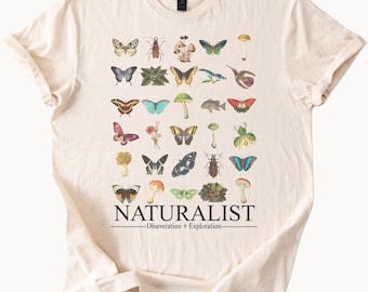 May include: A cream-coloured t-shirt displaying a detailed graphic of insects, butterflies, mushrooms, and plants. The word "NATURALIST" is printed below the illustrations, with the text "Obsevation + Exploration" underneath.