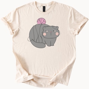 Funny grumpy gray cat tangled in yarn with pink cheeks cartoon style graphic cute animal humor t shirt for cat lovers and pet owners
