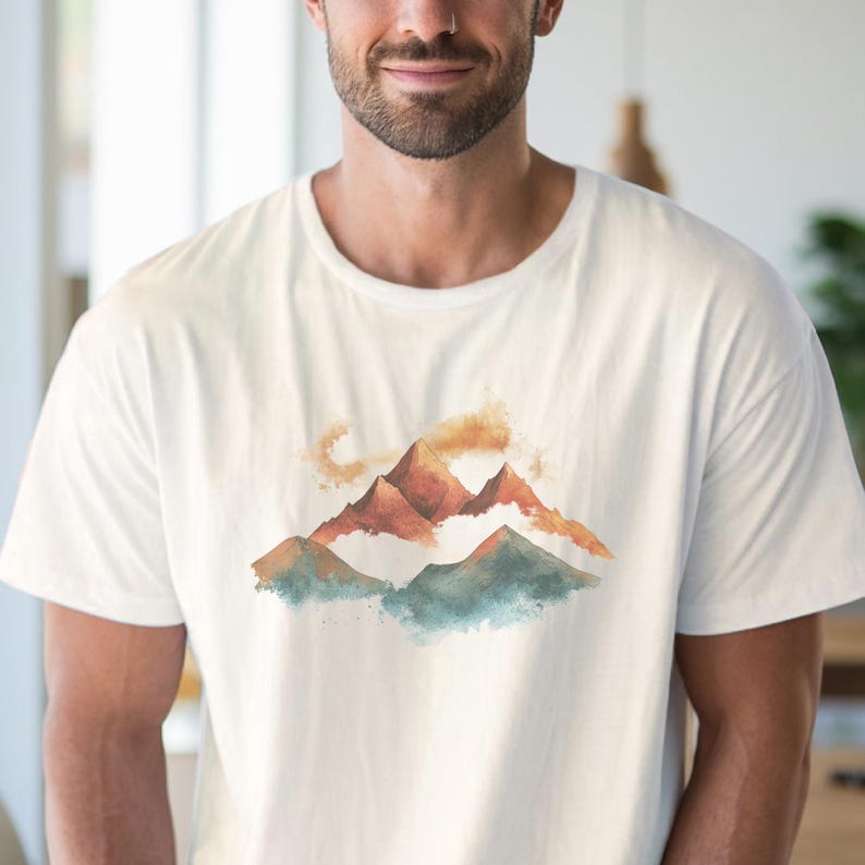 Op de afbeelding: Wit T-shirt met een aquarelontwerp van bergen en wolken in tinten bruin, oranje en blauw.