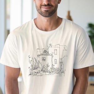 May include: Off-white t-shirt featuring a black and white line drawing of a building with potted plants. The illustration depicts a building with windows, a rooftop, and various plants in pots. The shirt is made of a soft, light-colored fabric.