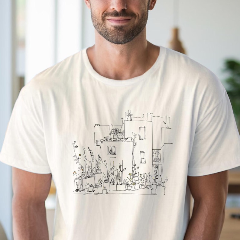 May include: Off-white t-shirt featuring a black and white line drawing of a building with potted plants. The illustration depicts a building with windows, a rooftop, and various plants in pots. The shirt is made of a soft, light-colored fabric.