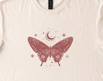 May include: A cream colored t-shirt with a red butterfly design. The butterfly has a crescent moon and stars above it.