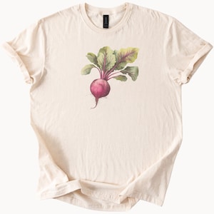 May include: A cream-coloured t-shirt displaying a watercolour illustration of a beetroot. The beetroot has a round, deep-red root, green and purple leaves, and a delicate root tail. The shirt has a classic crew neck and short sleeves.