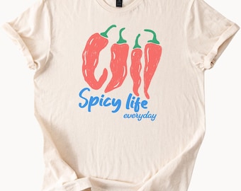 Op de afbeelding: Crèmekleurig T-shirt met een afbeelding van vier rode chilipepers met groene stelen. De woorden "Spicy life" in blauw en "everyday" in een kleinere blauwe letter staan eronder. Het shirt heeft korte mouwen.