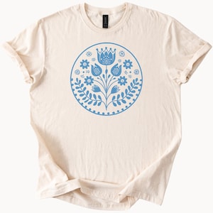 May include: A cream colored t-shirt with a blue floral design in a circle on the front.