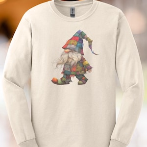 May include: Cream-colored long-sleeve shirt featuring a whimsical gnome illustration. The gnome is depicted in a patchwork outfit with a colorful hat and long white beard. The design is centered on the shirt, offering a playful and artistic aesthetic.