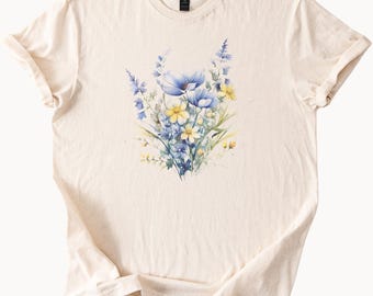 May include: Cream-colored t-shirt featuring a watercolor floral design. The design showcases a bouquet of blue and yellow flowers with green foliage. The shirt has a classic crew neck and short sleeves, perfect for casual wear.